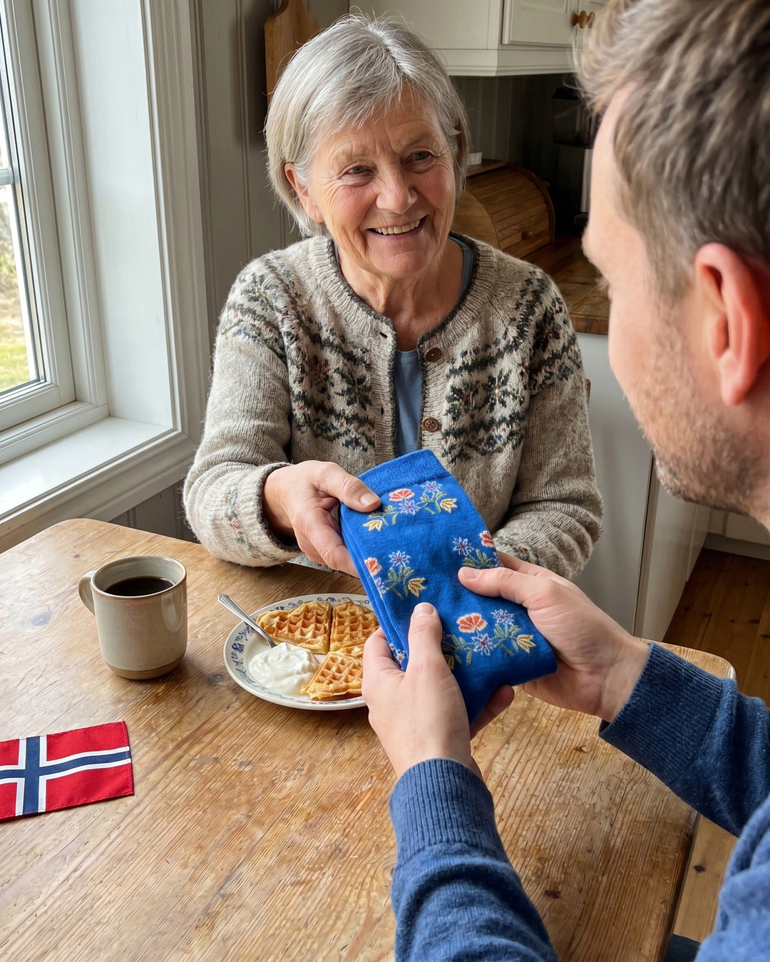 Mormor gir bunadsinspirerte Nordland-sokker til barnebarn ved kjøkkenbordet